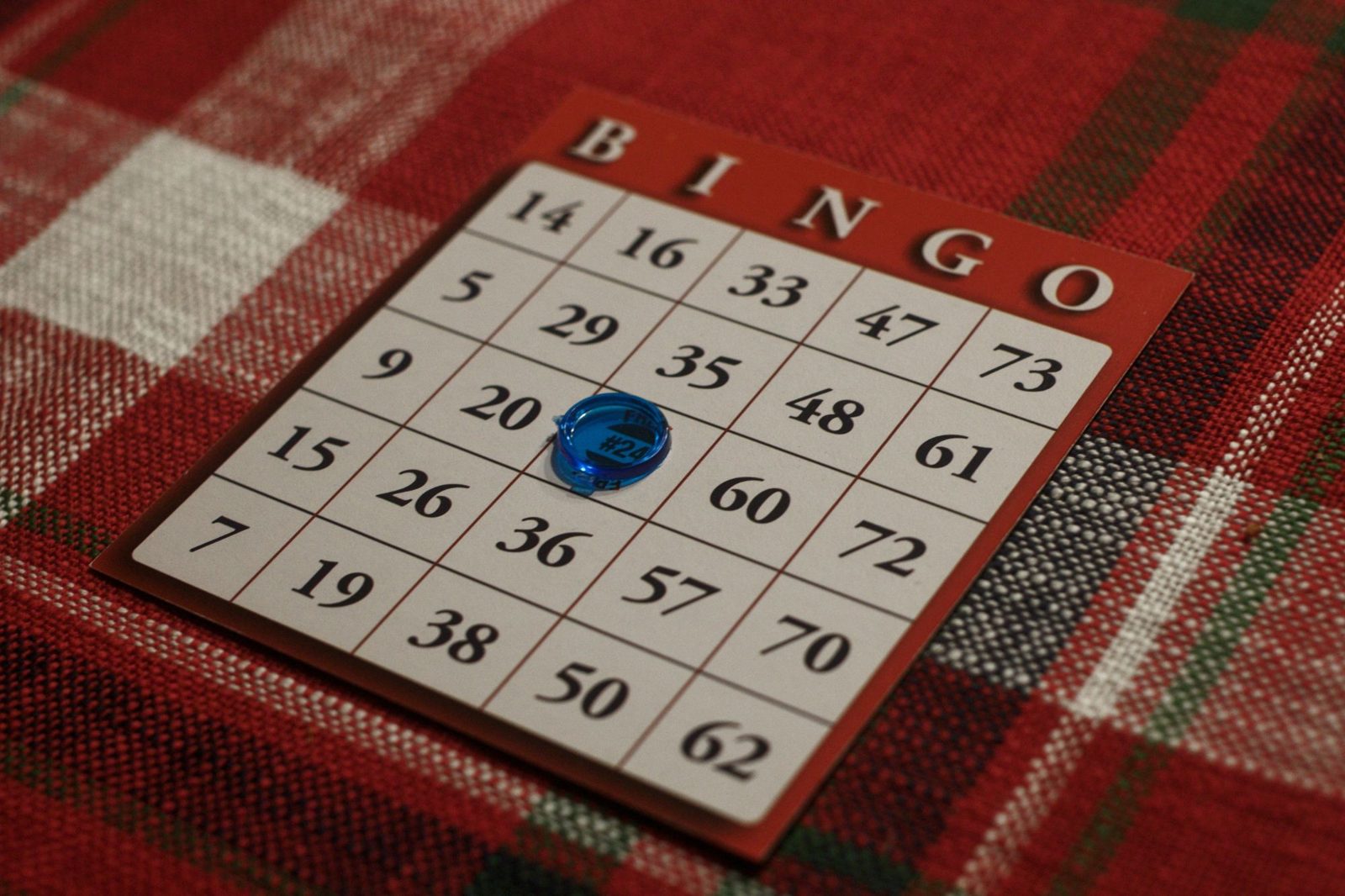 Cartón de bingo con una ficha azul marcada sobre un mantel de cuadros rojo