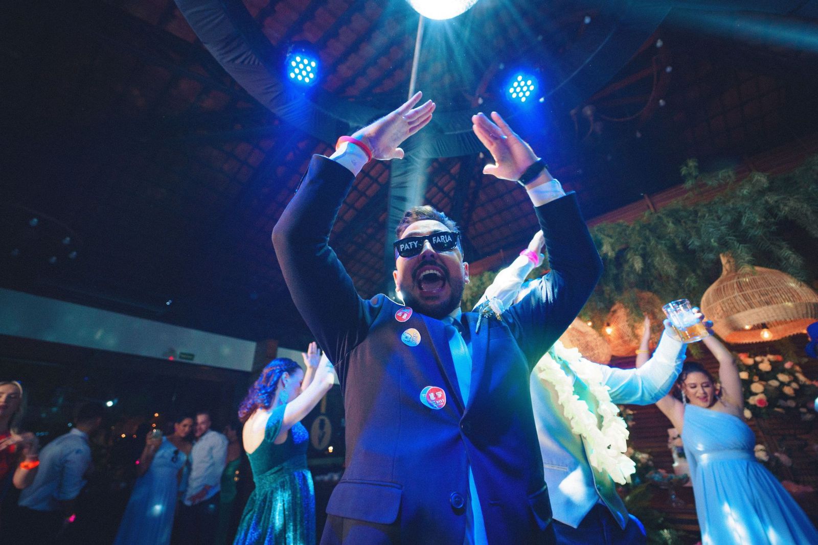 Invitados bailando con los brazos en alto en la barra libre de una boda, bajo luces azules y una bola de espejos